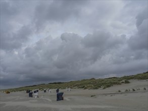 Empty beach with beach chairs, large dunes and dark grey clouds in the sky, juist, east frisia,