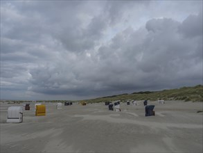 Extensive beach with colourful beach chairs, mighty dunes and dark clouds in the sky, juist, east