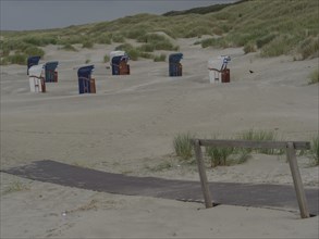 Beach with wooden path, several beach chairs and dunes, sand and cloudy sky, juist, east frisia,