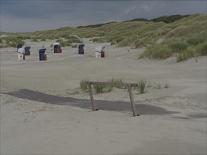 View of a beach with dunes and beach chairs in the background, wooden path embedded in the sand,