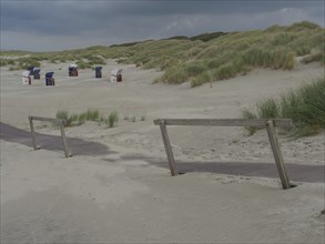 Deserted beach with a wooden path and scattered beach chairs under a cloudy sky, juist, east