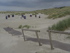 A beach with several beach chairs and a wooden path through the dunes under a cloudy sky, juist,