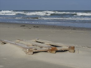 Old wooden pallets lying on the beach, with waves of the sea in the background, juist, east frisia,