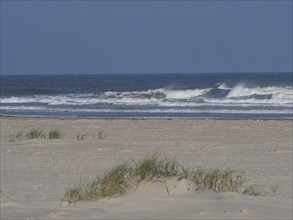 Quiet beach with dunes and grassy sand hills in front of the undulating sea, Juist, East Frisia,