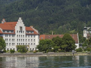 Historic buildings with red roofs and trees in front of a mountainous landscape, Lindau, Lake