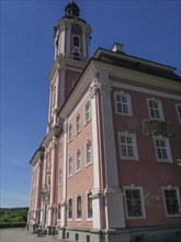 Large pink church façade with high windows under a blue sky in sunny weather, Meersburg, Germany,