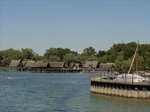 Pile dwellings on a lake with boats and a jetty, surrounded by nature in summer under a blue sky,