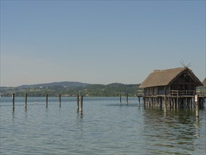 Wooden house on stilts on a quiet lakeshore with a hilly landscape in the background, Meersburg,