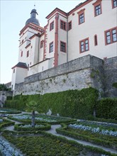 A historic castle with red and white buildings, surrounded by stone walls and manicured green