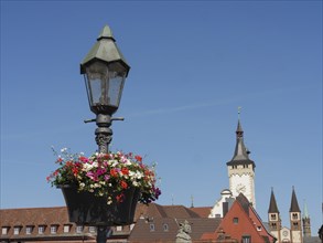 Hanging lamp with blossoming flowers in the foreground, church tower and historic buildings in the