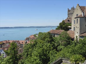 A castle and surrounding buildings on the lakeshore with lush greenery and red roofs, Meersburg,