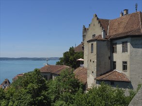 A medieval castle on the shore of a lake, surrounded by trees, overlooking calm waters in sunny