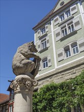 A bear statue on a column in front of a historic building with green plaster and overgrown walls