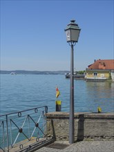 Idyllic view of a lake with a lantern and a railing in the foreground and houses and a boat in the