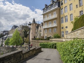 Curve of an urban street with yellow buildings and overgrown pavement, cloudy sky, Luxembourg City,