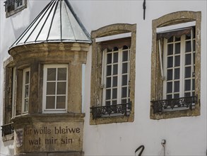 Historic façade with bay window and inscription, rustic stone frames around windows, traditional