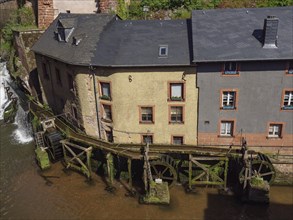 Close-up of a watermill with old buildings on the river, wooden mechanism visible, Saarburg,