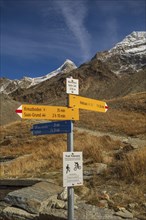 A signpost on a hiking trail in the mountains under a clear blue sky, surrounded by dry landscape