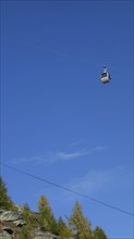 A cable car in front of a bright blue sky over an autumn-coloured mountain, Saas Fee, Switzerland,