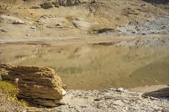 Calm lake with rocky shore and reflecting cliffs in a desert landscape, Grisons, Switzerland,