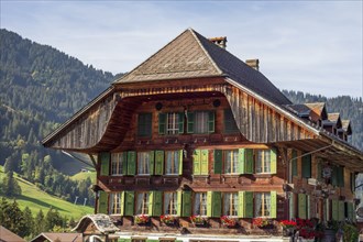 Red wooden house in the Alps with green shutters and flower boxes, surrounded by mountains in the