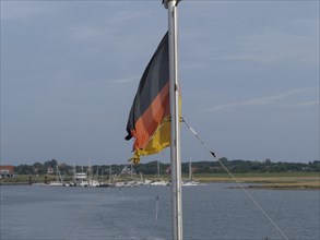 A German flag on a boat, surrounded by water and a quiet harbour, Spiekeroog, East Frisia, GERMANY