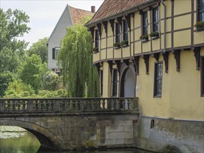 Historic building on the waterfront with a bridge, willow and flowering windowsills, Steinfurt,