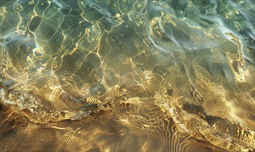 Clear water reflecting sunlight on a beach, creating ripples and patterns on the golden sand