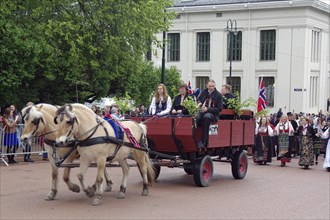 Horse-drawn carriage with traditionally dressed people at a Norwegian parade in front of a central