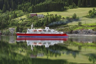 A cruise ship is reflected on a calm fjord in front of a green landscape, Nordfjord, Loen, Norway,