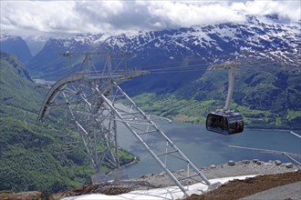 Modern cable car crossing a fjord and green valleys with snow-capped mountains in the background,