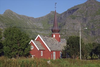 Red church with tower surrounded by trees and mountains under a clear blue sky, onion dome,