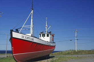 Red boat on land next to a coastal road under a clear blue sky, Gaspesie, St. Lawrence River,