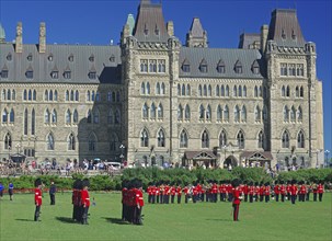 A group of uniformed soldiers march in front of a historic parliament building in sunny weather,