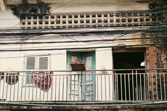 Facade of an old, dilapidated building with peeling paint, a balcony with hanging clothes, and