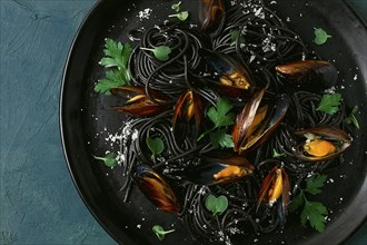 Spaghetti with black squid, black pasta, with boiled mussels, on a black plate, with parsley and