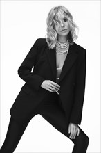 A beautiful woman with loose hair, in a jacket and beads, poses in the studio on a white background