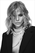 A beautiful woman with loose hair, in a jacket and beads, poses in the studio on a white background