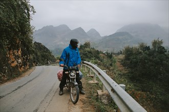 Person in a blue jacket and helmet on a motorcycle stopped on a foggy mountain road taking the