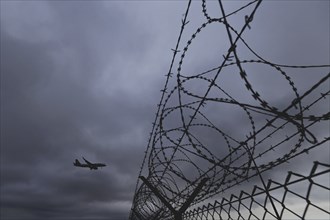 An aircraft looms over a barbed wire fence, taken at Berlin Brandenburg Airport 'Willy Brandt'Äô