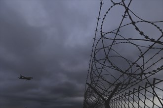 An aircraft looms over a barbed wire fence, taken at Berlin Brandenburg Airport 'Willy Brandt'Äô