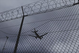 An aircraft looms over a barbed wire fence, taken at Berlin Brandenburg Airport 'Willy Brandt'Äô