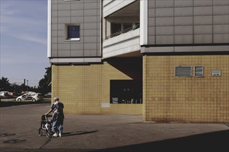 An old woman with a walking frame stands out in front of a block of flats in Marzahn, taken in