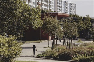 A boy with a football stands out in a green area between blocks of flats in Marzahn, taken in