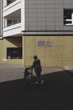 An old woman with a walking frame stands out in front of a block of flats in Marzahn, taken in