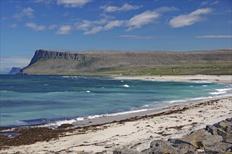 A clear day on a sandy beach with waves crashing against the shore and sapphire blue water,