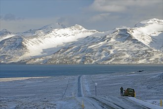 Snowy road leading to a lake, surrounded by mountains, with a car on the edge of the winter