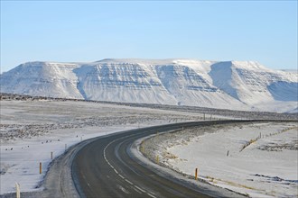 Snowy road leads to a snow-covered mountain range under a clear blue sky, Ring Road, North Iceland,