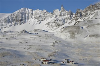 Snow-covered mountains with small houses in the foreground under a clear blue sky, winter,