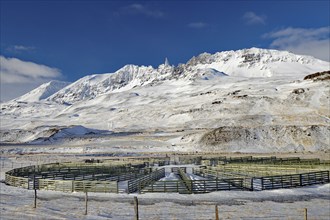 Snow-covered mountains behind a circular fence under a blue sky, winter, Öxnadalur, Akureyri,